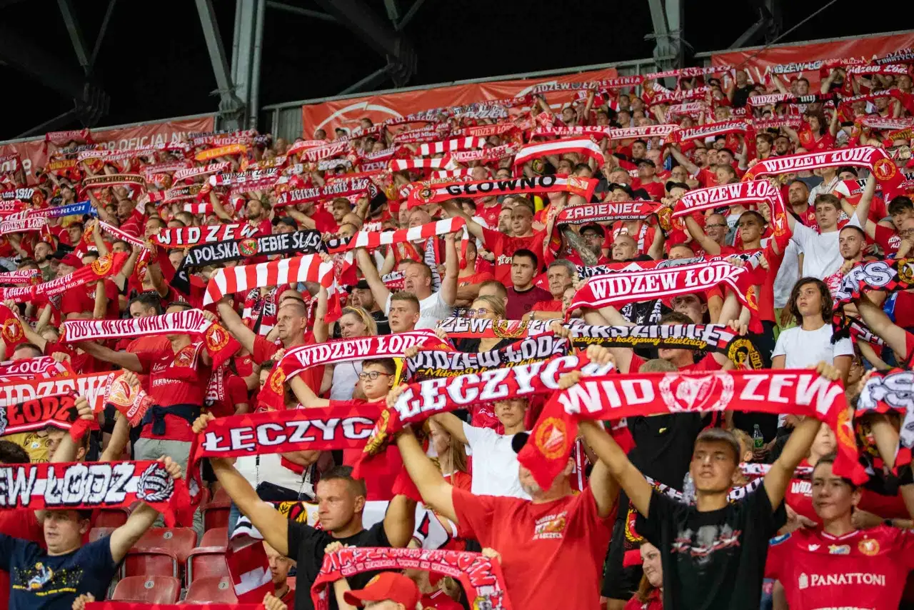 Tysiące kibiców na stadionie, wszyscy w czerwonych szalikach z napisami 