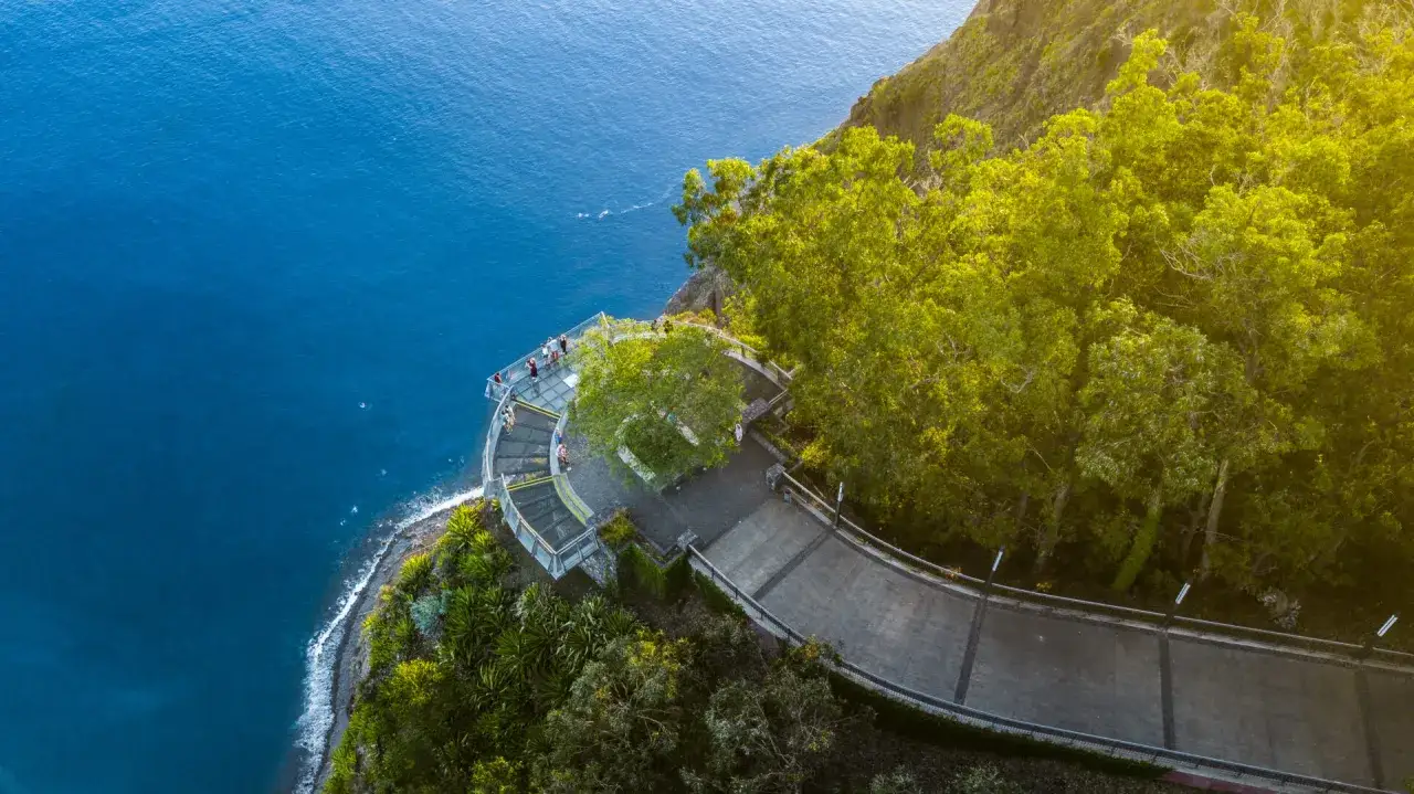 Blick von oben auf die Glasplattform Cabo Girao mit Menschen, die die Aussicht auf das tiefblaue Meer genießen.