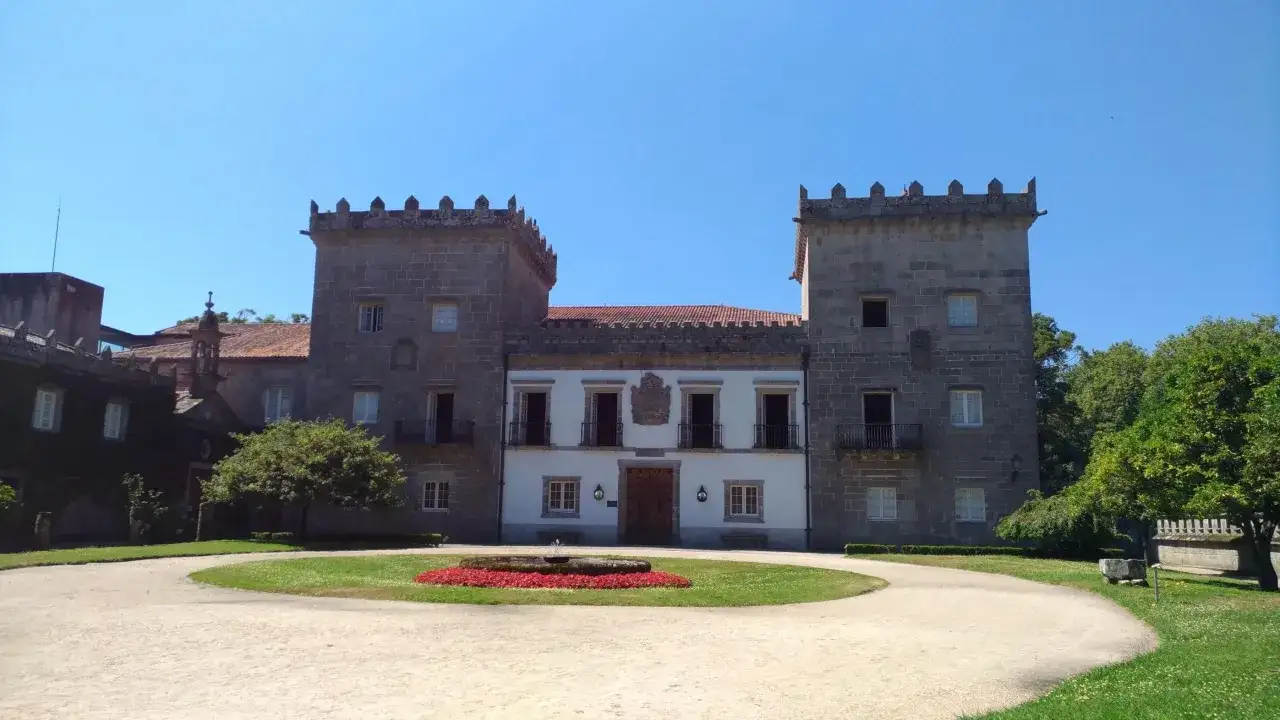 Edificio señorial con torres almenadas en el parque de Castrelos, con una fuente y flores rojas en el centro de un jardín circular.