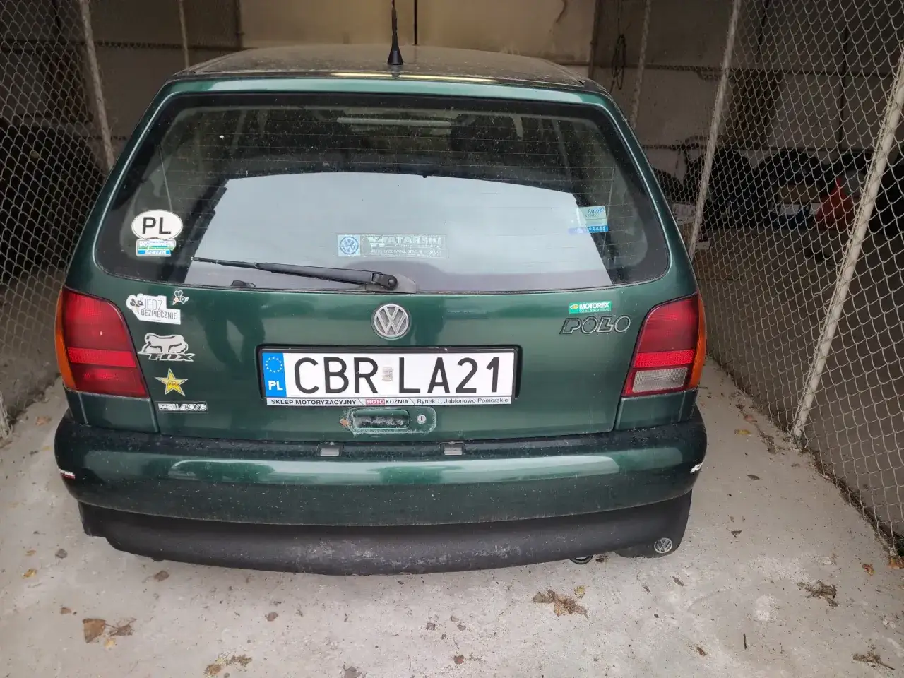Zielony Volkswagen Polo z tablicą rejestracyjną CBR LA21, ozdobiony naklejkami, stoi w garażu.