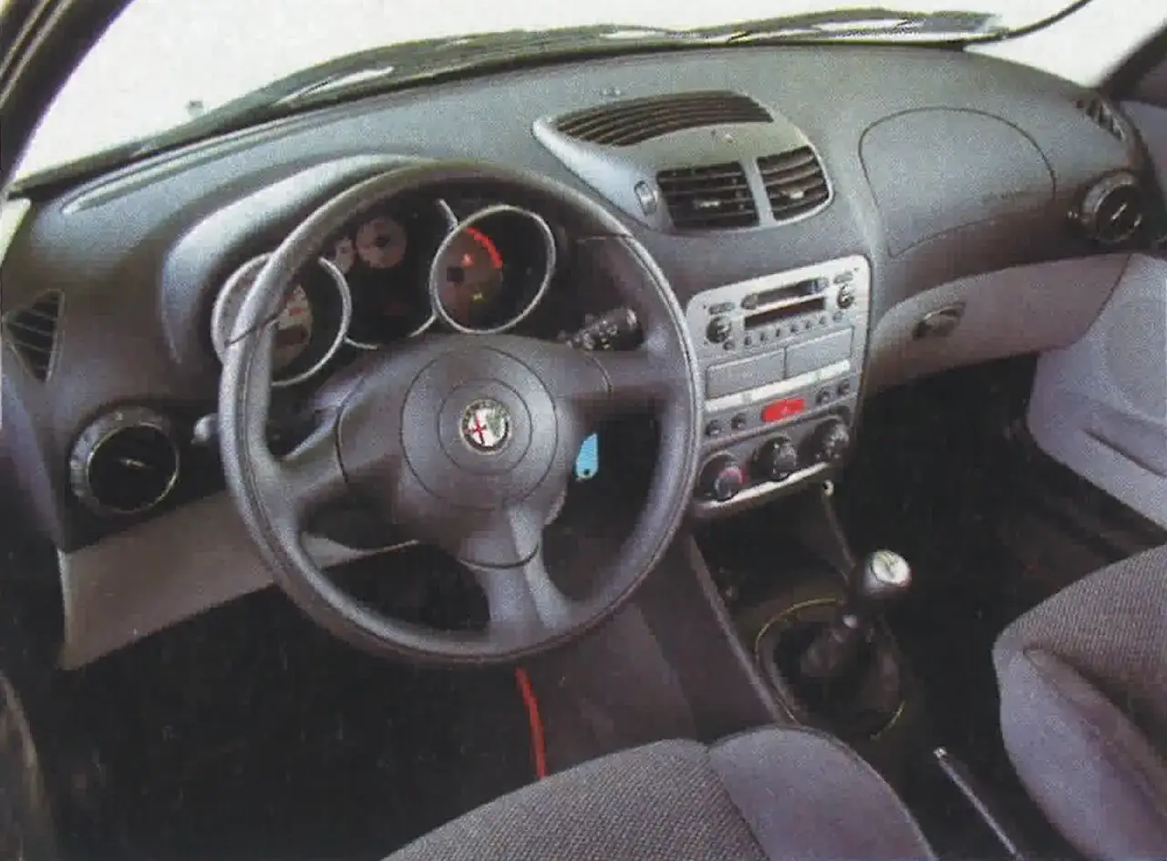 Wnętrze Alfa Romeo 147 1.9 JTD: kierownica, deska rozdzielcza z radiem i nawiewami, dźwignia zmiany biegów.