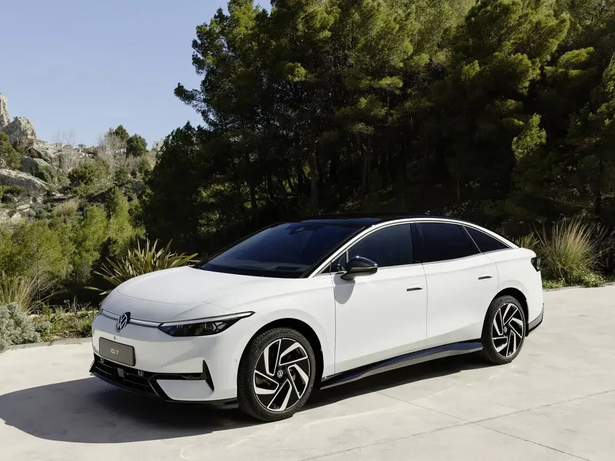 El Volkswagen ID.7 blanco, con su techo negro, descansa en un camino de concreto, rodeado de exuberante vegetaci&oacute;n y colinas rocosas.