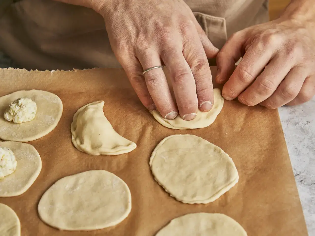 H&auml;nde formen Teigkreise f&uuml;r ein Piroggen Rezept. Einige sind bereits gef&uuml;llt, andere warten auf ihre F&uuml;llung.