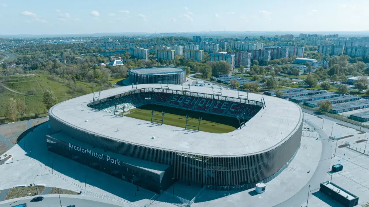 Widok z lotu ptaka na nowoczesną arenę w Sosnowcu, otoczoną zielenią i zabudowaniami miejskimi.