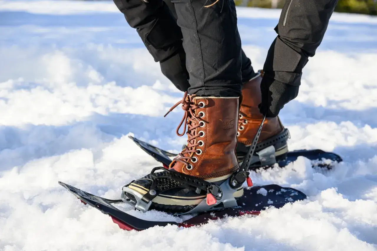 Lace-up brown boots are secured to snowshoes, ready for a winter trek. You don't need special boots for snowshoes; sturdy winter boots work well.