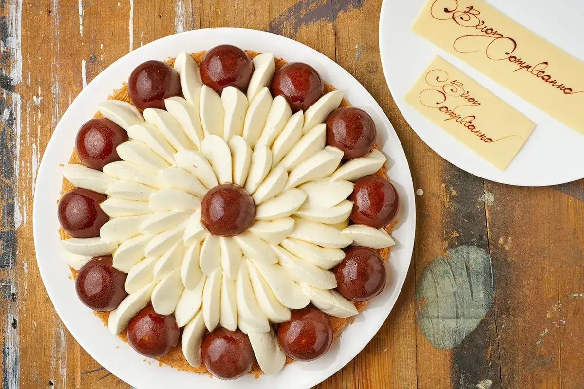 Torta floreale con sfere di cioccolato e panna montata, perfetta tra i dolci per compleanno adulti. Due tavolette di cioccolato con la scritta 