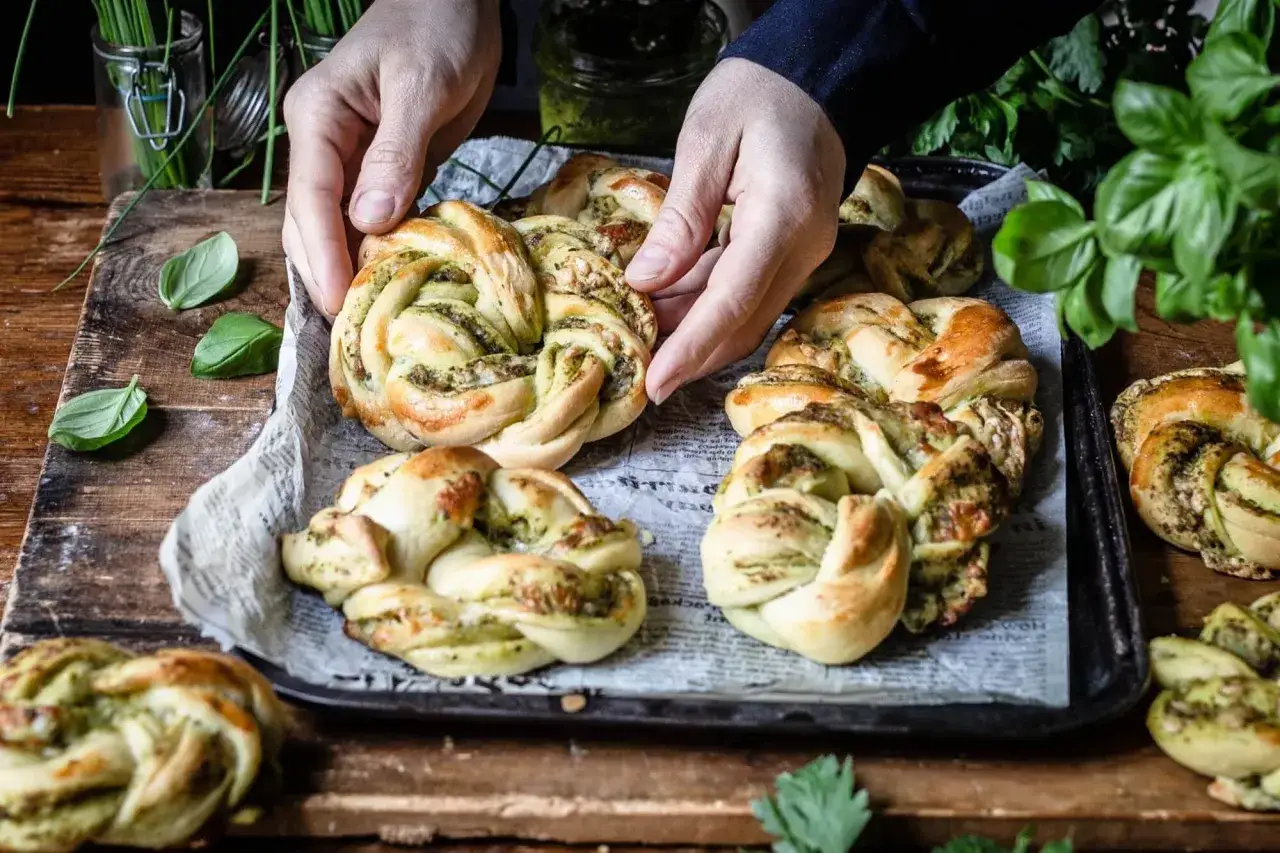 H&auml;nde greifen nach frisch gebackenen Zopfbr&ouml;tchen mit Pesto, inspiriert von herzhaften Rezepten mit Mais.