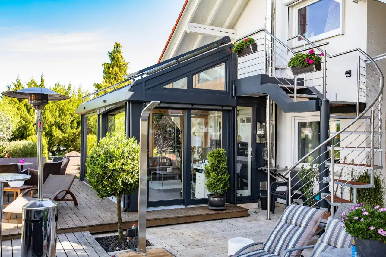 Moderner Wintergarten mit Außentreppe und Heizstrahler. Perfekt für gemütliche Abende im Freien, auch wenn es draußen kalt ist.