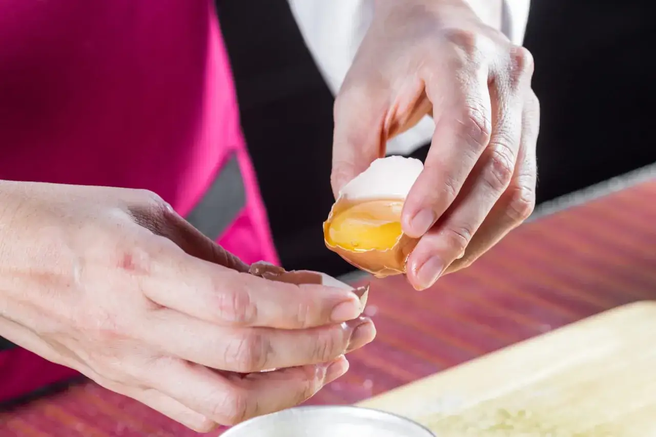 Mains s&eacute;parant d&eacute;licatement le jaune d'&oelig;uf blanc de sa coquille.