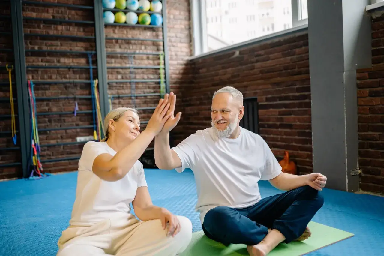 Ett leende par ger varandra high-five efter ett lyckat senior yoga-pass i gymmet.