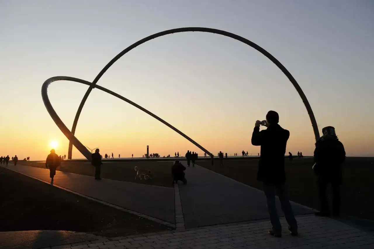 Sonnenuntergang am Halde Rungenberg Parken. Menschen spazieren unter riesigen Stahlbögen, ein Fotograf hält den Moment fest.