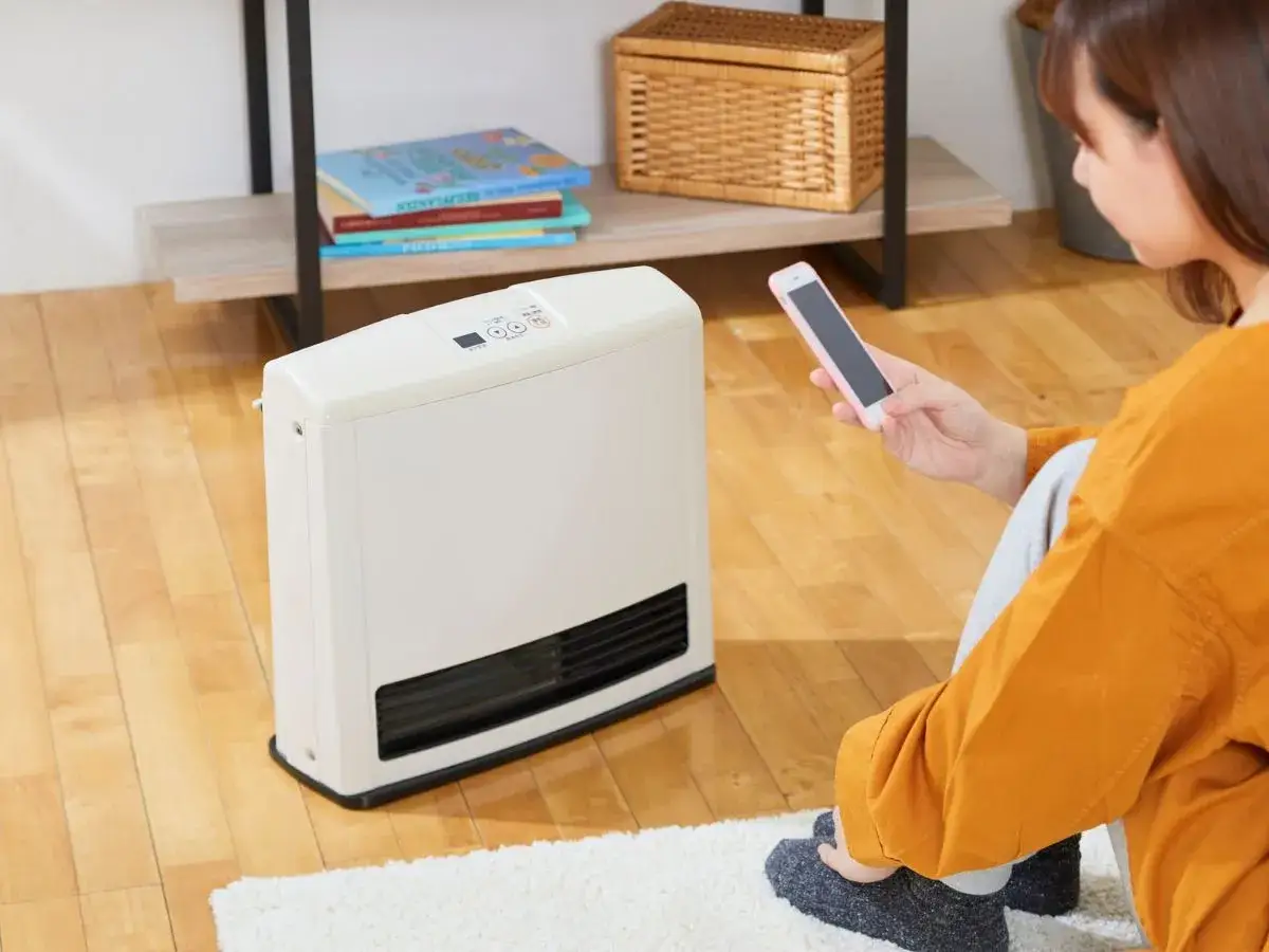 Donna controlla i **sistemi di riscaldamento elettrici** tramite smartphone, seduta sul tappeto accanto al calorifero.