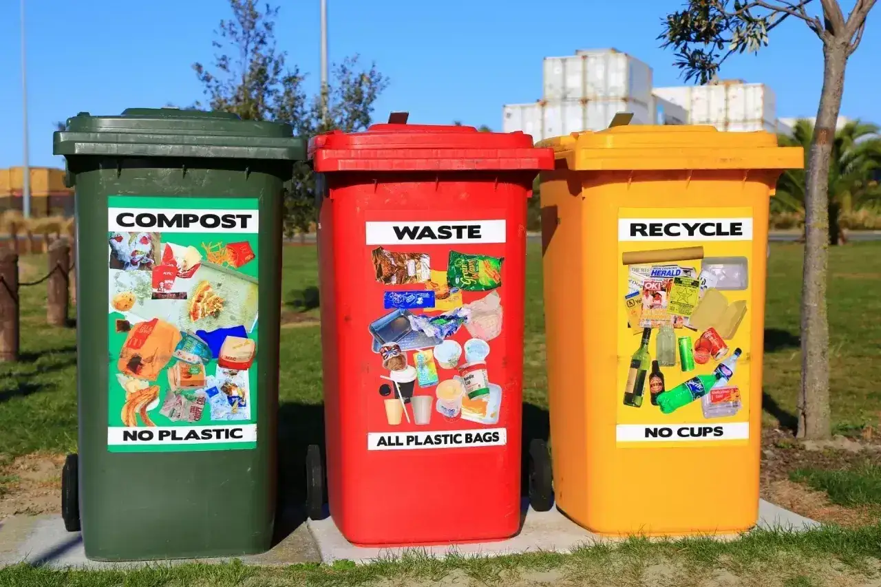 Trzy kosze na śmieci: zielony (kompost, bez plastiku), czerwony (odpady, wszystkie plastikowe torby) i żółty (recykling, bez kubków). Przykłady opakowań z tworzyw sztucznych na naklejkach.