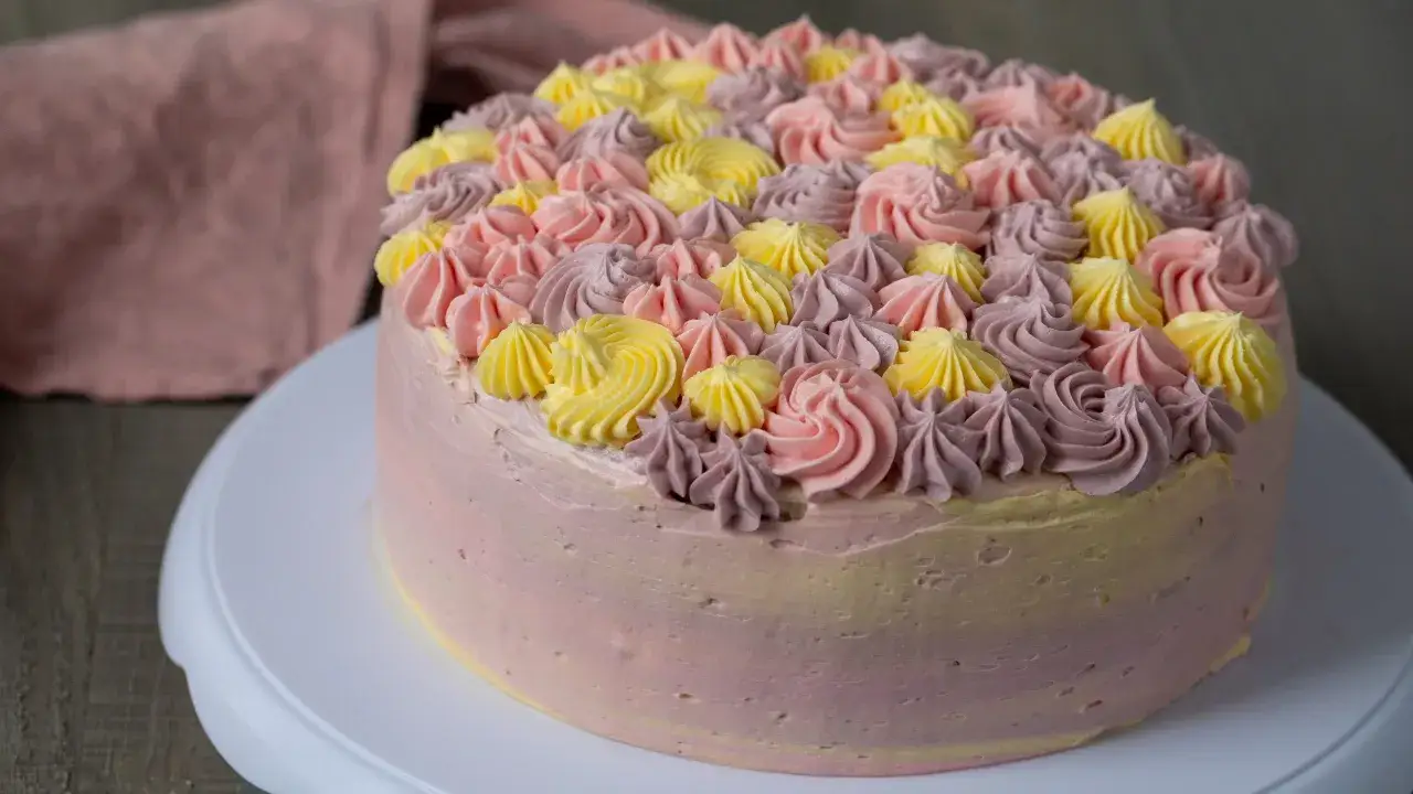 En vacker t&aring;rta med rosa, lila och gula frosting-rosetter p&aring; toppen. Perfekt f&ouml;r ett sommarfirande, inspirerad av ett enkelt frosting recept.
