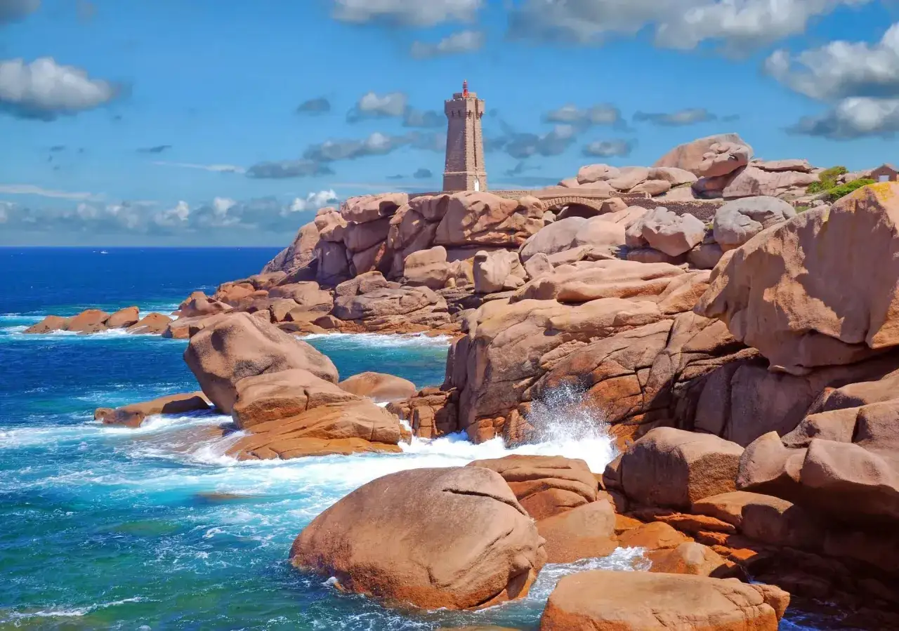Leuchtturm auf felsiger K&uuml;ste, ideal zum Wandern in der Bretagne. T&uuml;rkisblaues Meer bricht sich an roten Felsen.
