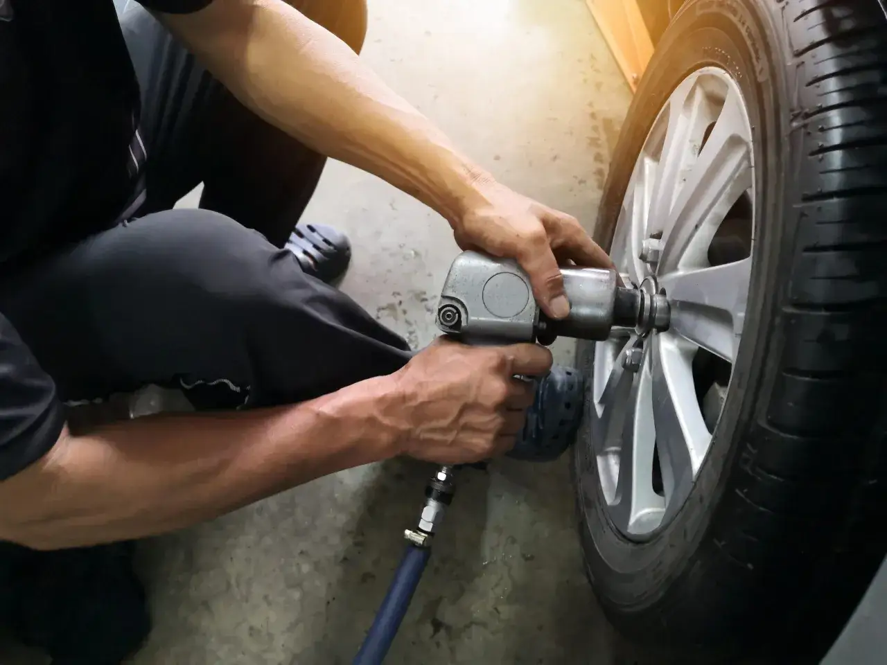 Mechanik dokręca śruby kluczem pneumatycznym. Zastanawiasz się, ile kosztuje wymiana opon?