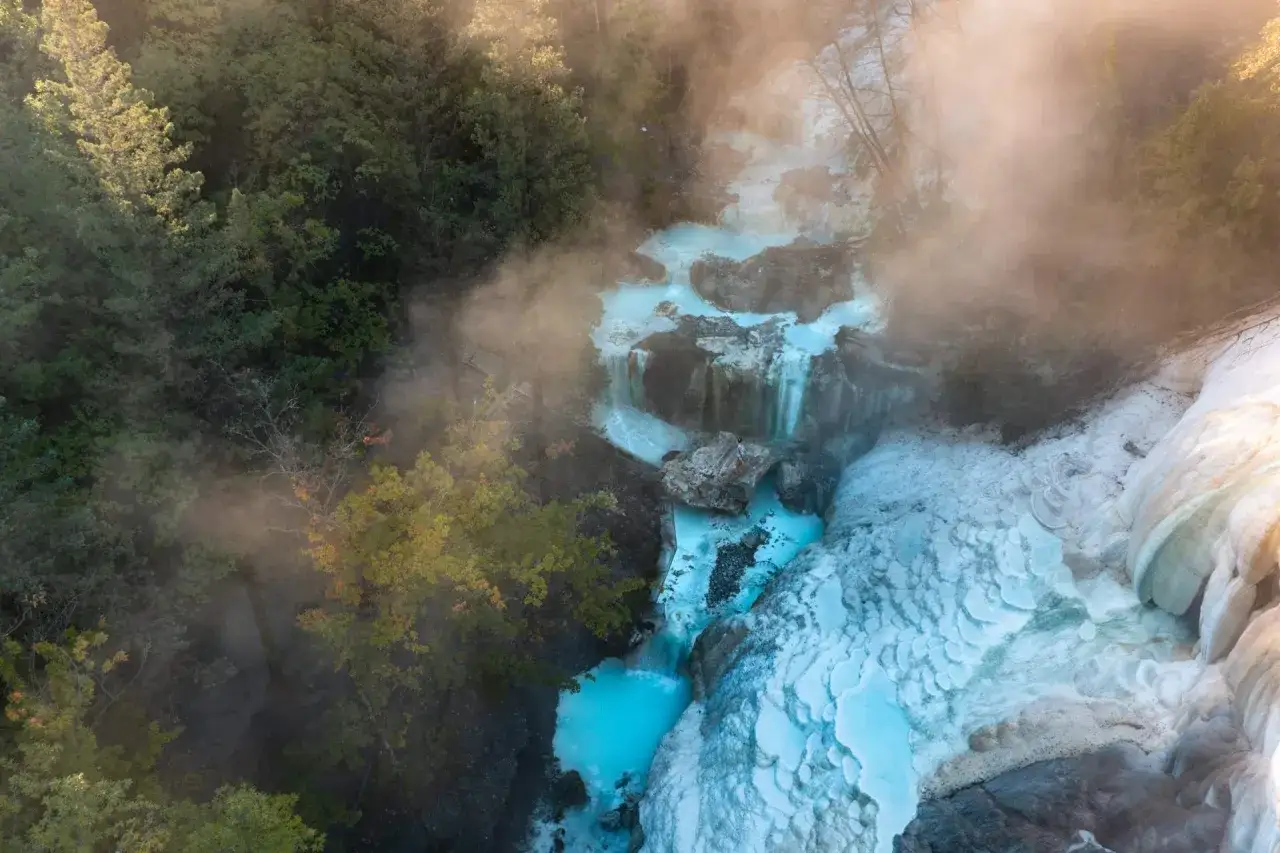 Cascades d'eau turquoise et formations calcaires spectaculaires aux Bagni San Filippo, baignées de vapeur et entourées de verdure.