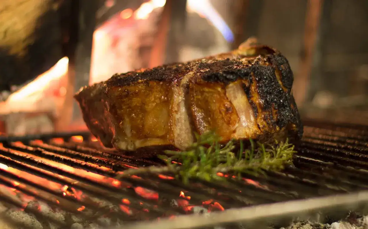 Bistecca alla fiorentina che cuoce sulla brace, un'esperienza da provare per chi cerca dove mangiare la fiorentina a Firenze.