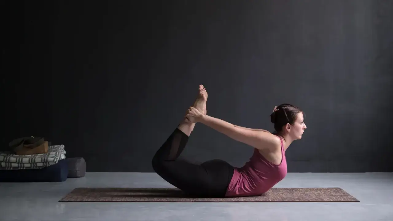 Mujer en postura del arco yoga (Dhanurasana), arqueando su espalda y sujetando sus tobillos.