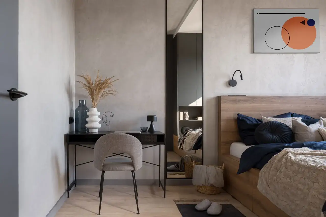 Un angolo studio in camera da letto con scrivania nera, sedia grigia, vasi e un letto accogliente.
