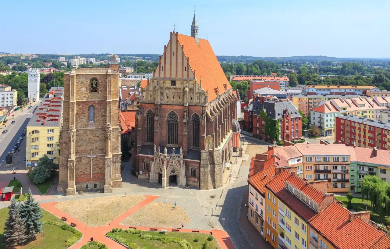 Nysa atrakcje: imponująca bazylika i wieża obok, otoczone kolorowymi kamienicami i zielenią.