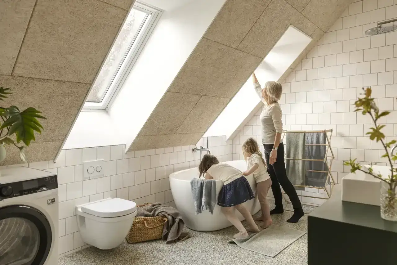 Salle de bain sous pente avec baignoire, WC suspendu, lave-linge et deux enfants curieux.