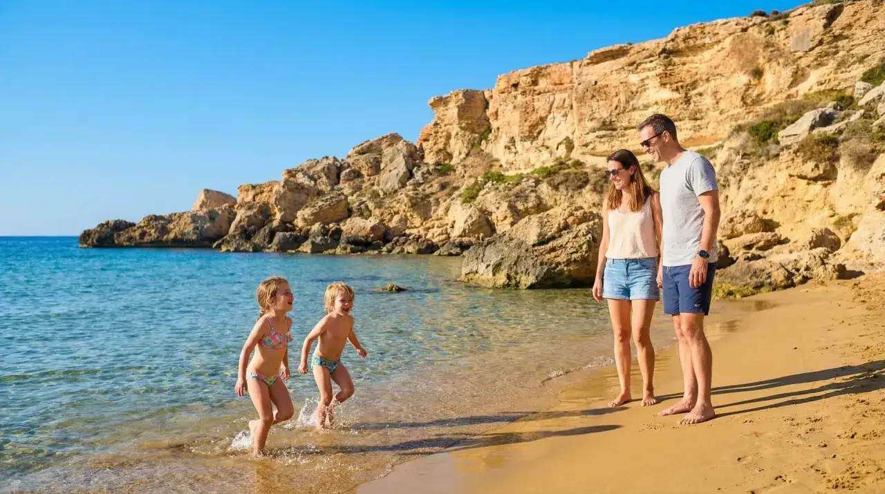Familie genießt einen sonnigen Tag am Strand auf Malta. Zwei Kinder planschen im Wasser, während die Eltern zusehen.
