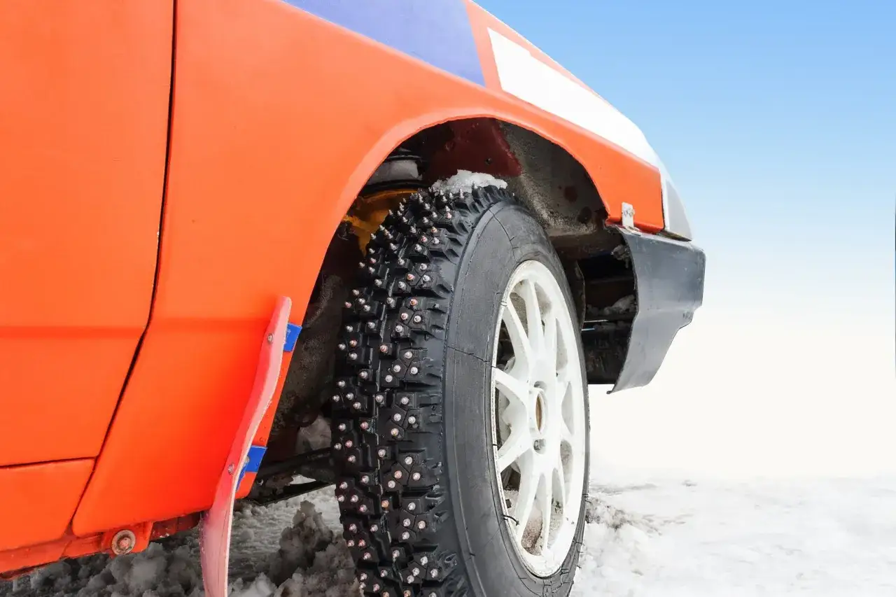 Ruota di un'auto arancione da rally con pneumatici chiodati pronti per affrontare la neve e il ghiaccio.