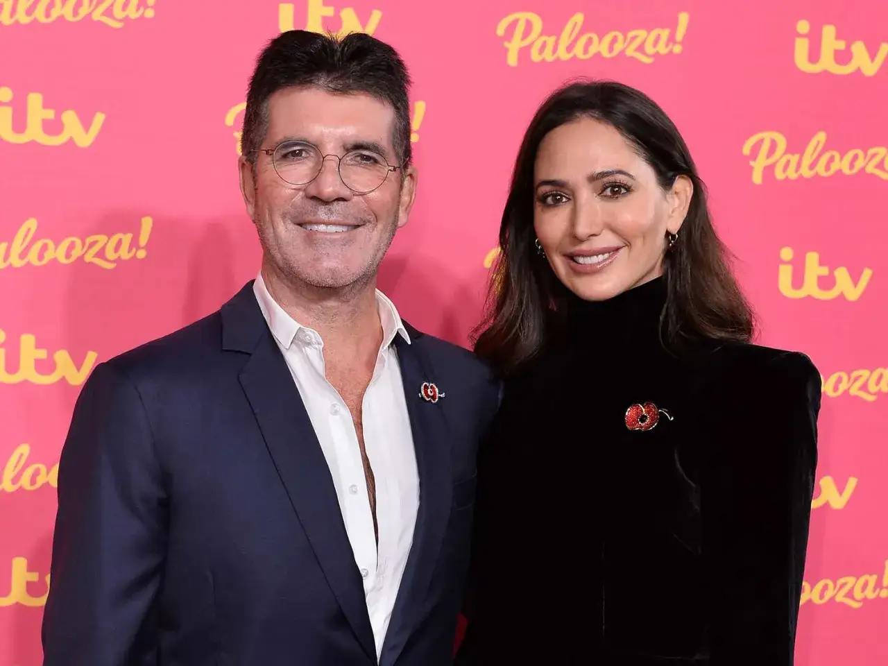 Simon Cowell och Lauren Silverman ler mot kameran p&aring; en rosa bakgrund med 
