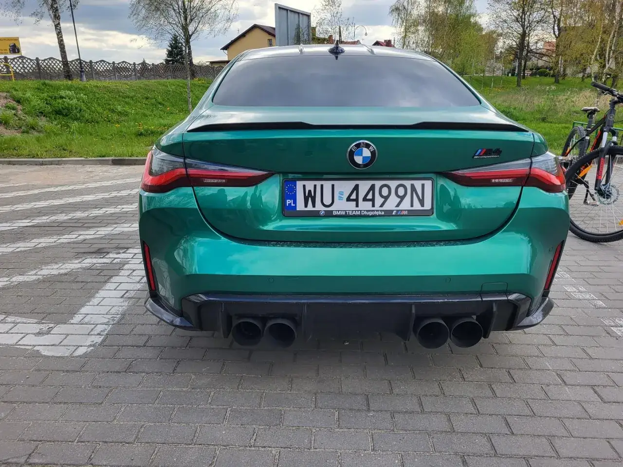 Zielone BMW M4 z tablicą rejestracyjną WU 4499N, zaparkowane obok roweru.