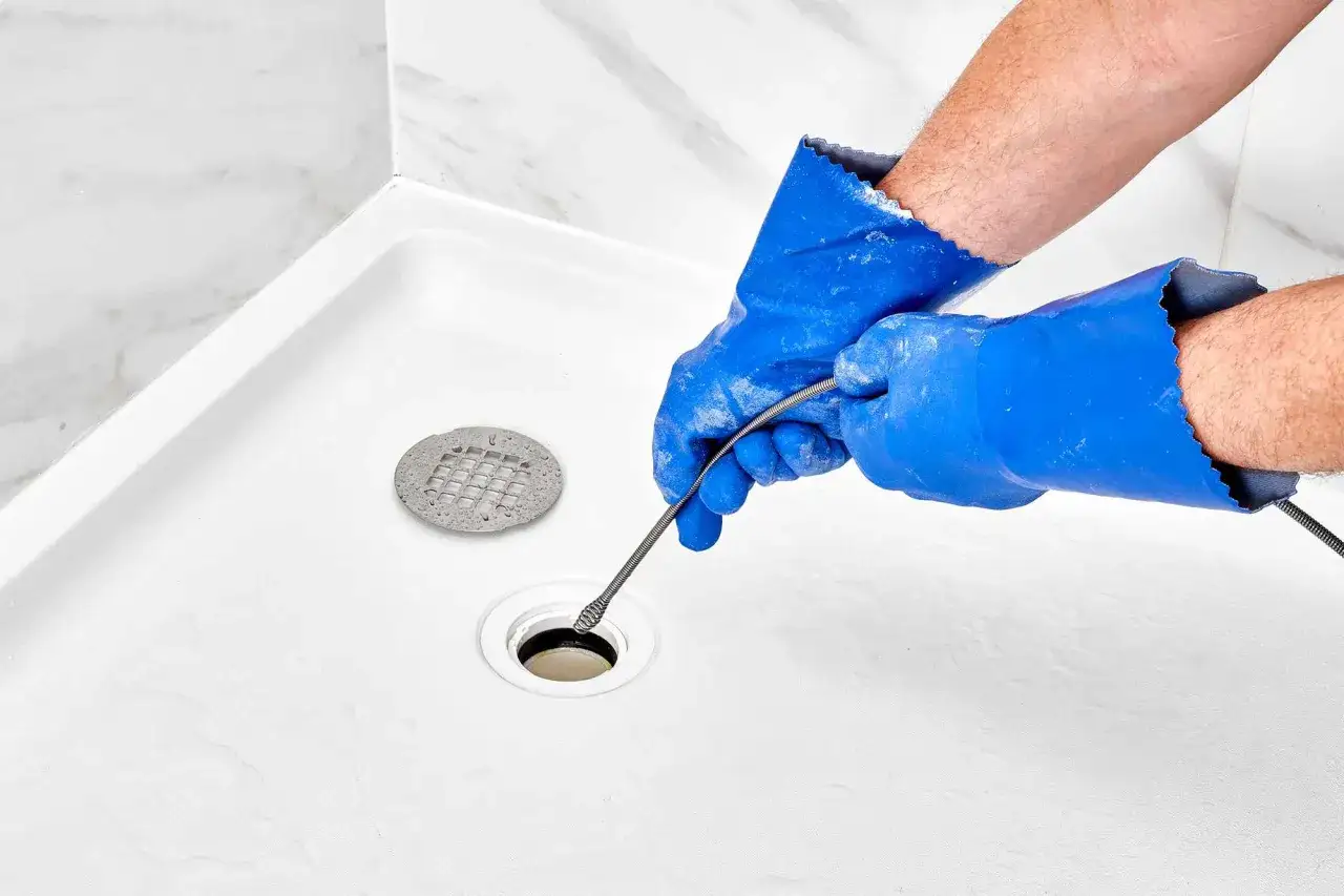 Mains bleues, outil de plomberie dans une douche blanche pour d&eacute;boucher la douche.