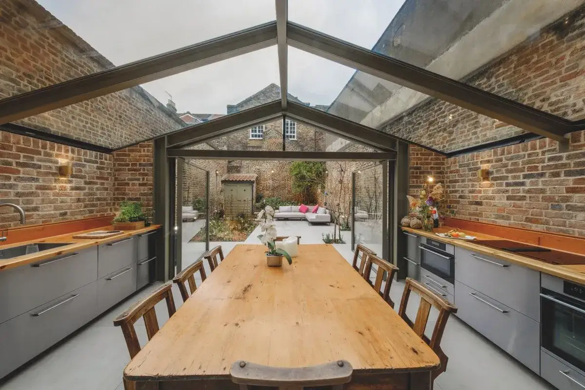 Une cuisine moderne avec une extension vitr&eacute;e toit plat, donnant sur un jardin avec salon de jardin.
