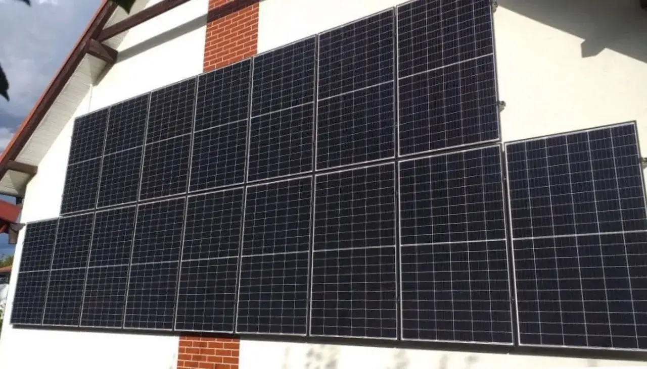 Duży zestaw paneli fotowoltaicznych na pionowej ścianie domu, zbierających energię słoneczną.