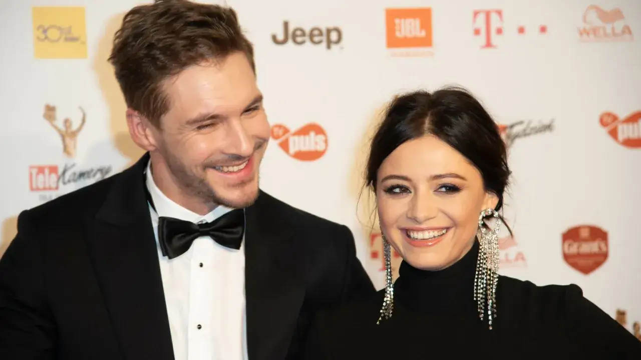Adriana Kalska i jej partner, Mikołaj Roznerski, uśmiechają się do obiektywu na tle ścianki z logotypami.