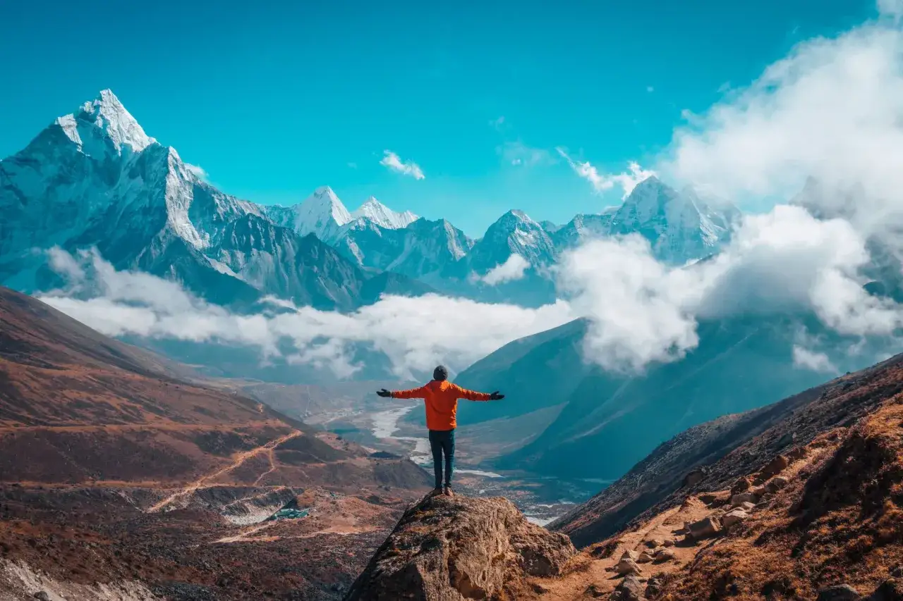 Widok na majestatyczne g&oacute;ry Himalaj&oacute;w, człowiek na szczycie skały z rozłożonymi rękami. Podr&oacute;ż na Everest Base Camp, poznaj jej koszty.