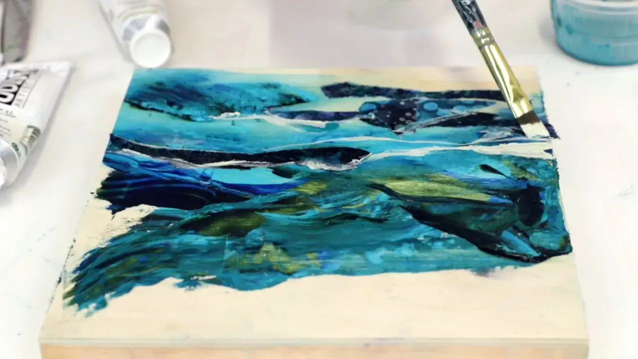Application de peinture acrylique et de résine sur une œuvre abstraite aux tons bleus et verts.