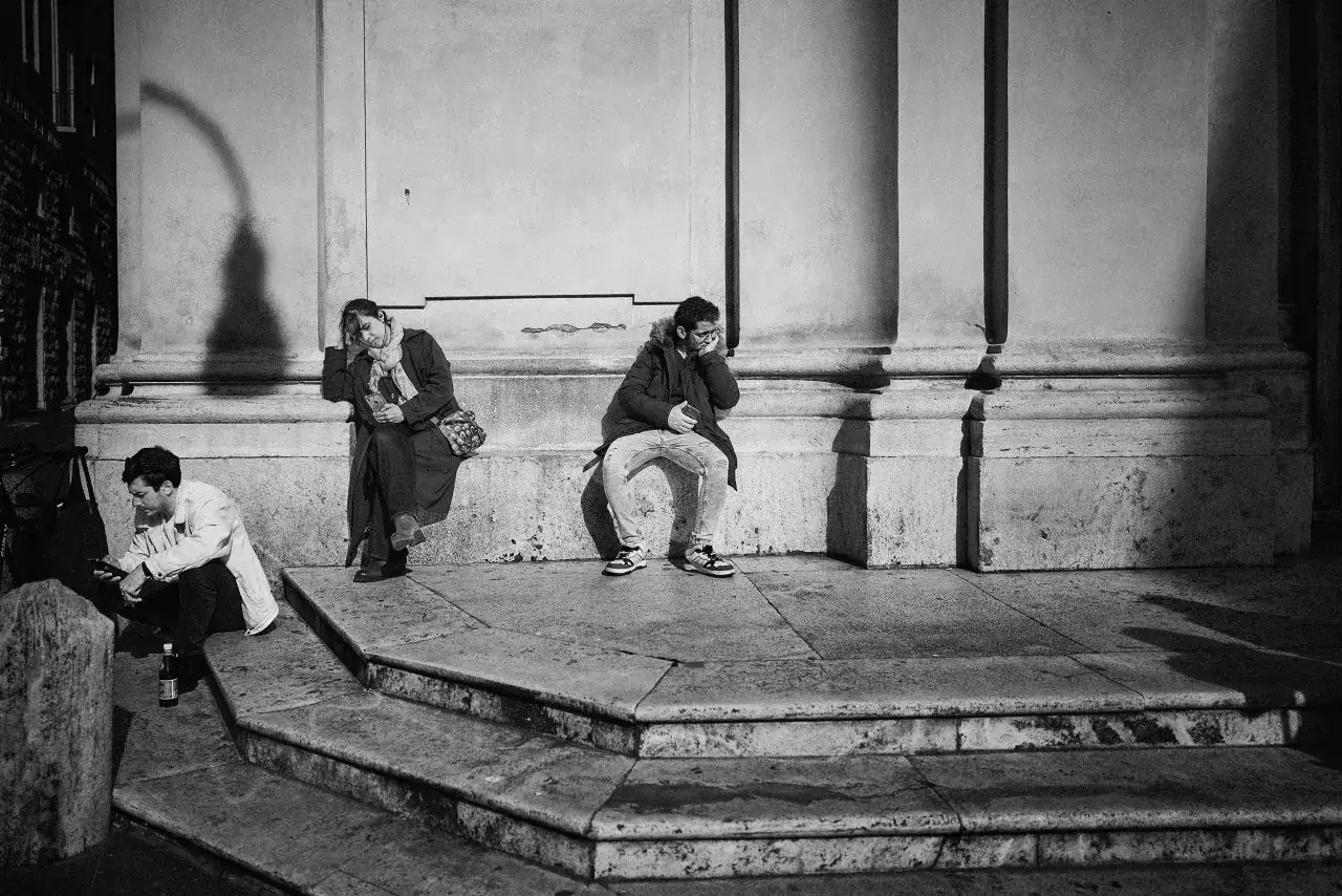 Tre persone sedute sui gradini, ognuna persa nei propri pensieri. Un racconto fotografico di momenti sospesi.