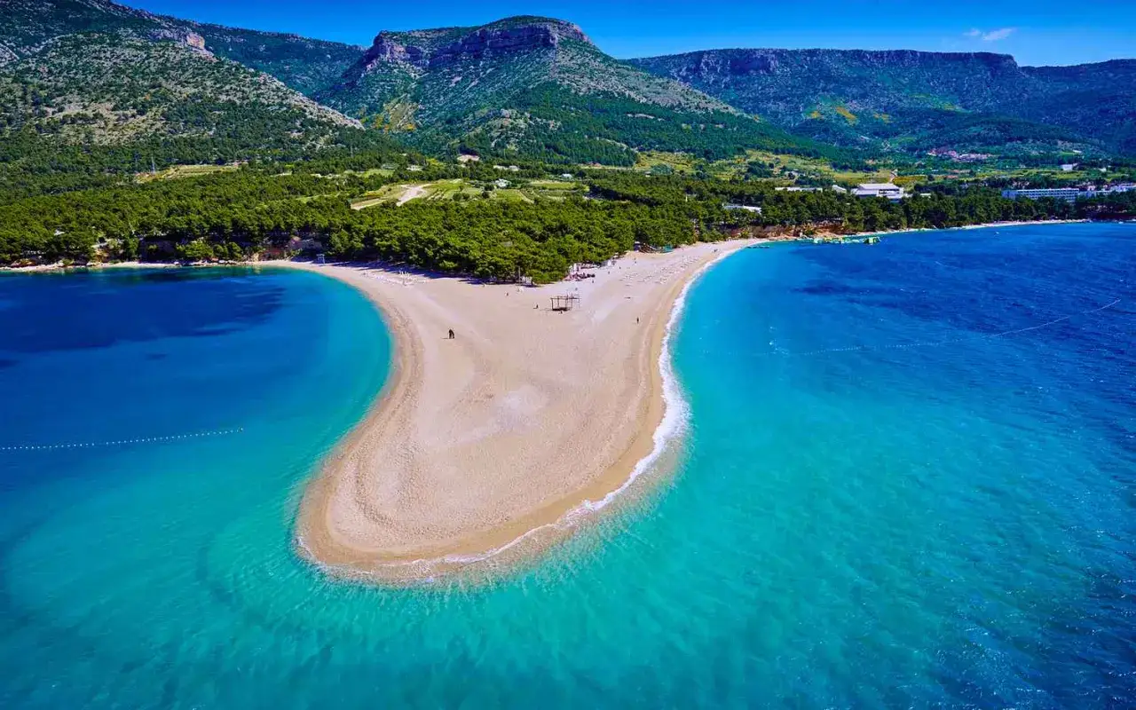 Zlatni Rat, jedna z najpiękniejszych plaż w Chorwacji, rozciąga się w turkusowych wodach Adriatyku, otoczona zielonymi wzgórzami.