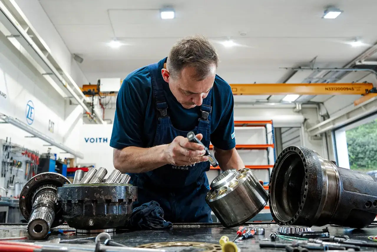 Doświadczony tokarz bada precyzyjnie elementy mechaniczne, oświetlając je latarką.