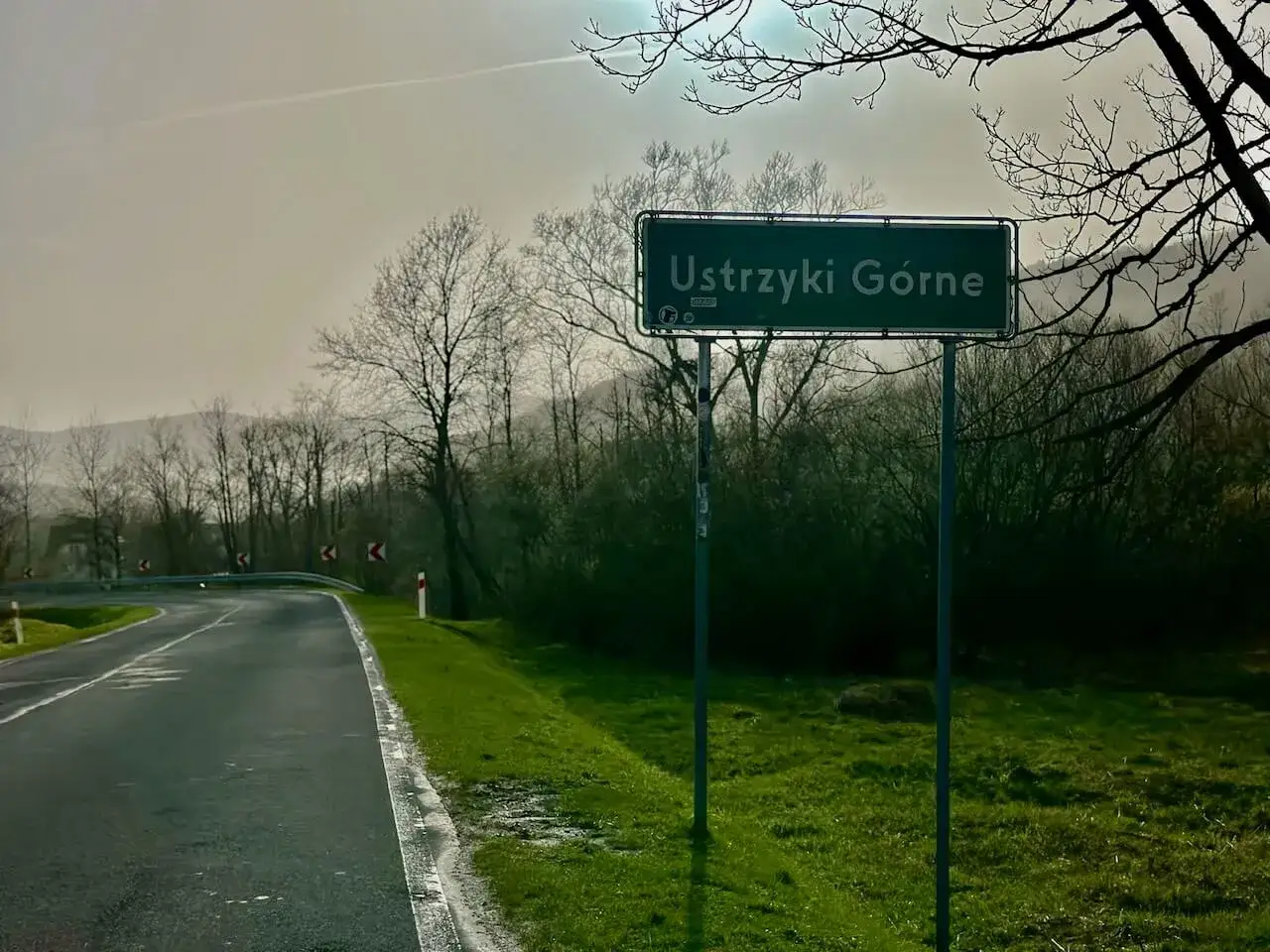 Droga z Krakowa do Ustrzyk Górnych. Znak z nazwą miejscowości Ustrzyki Górne na tle drzew i mglistego krajobrazu.