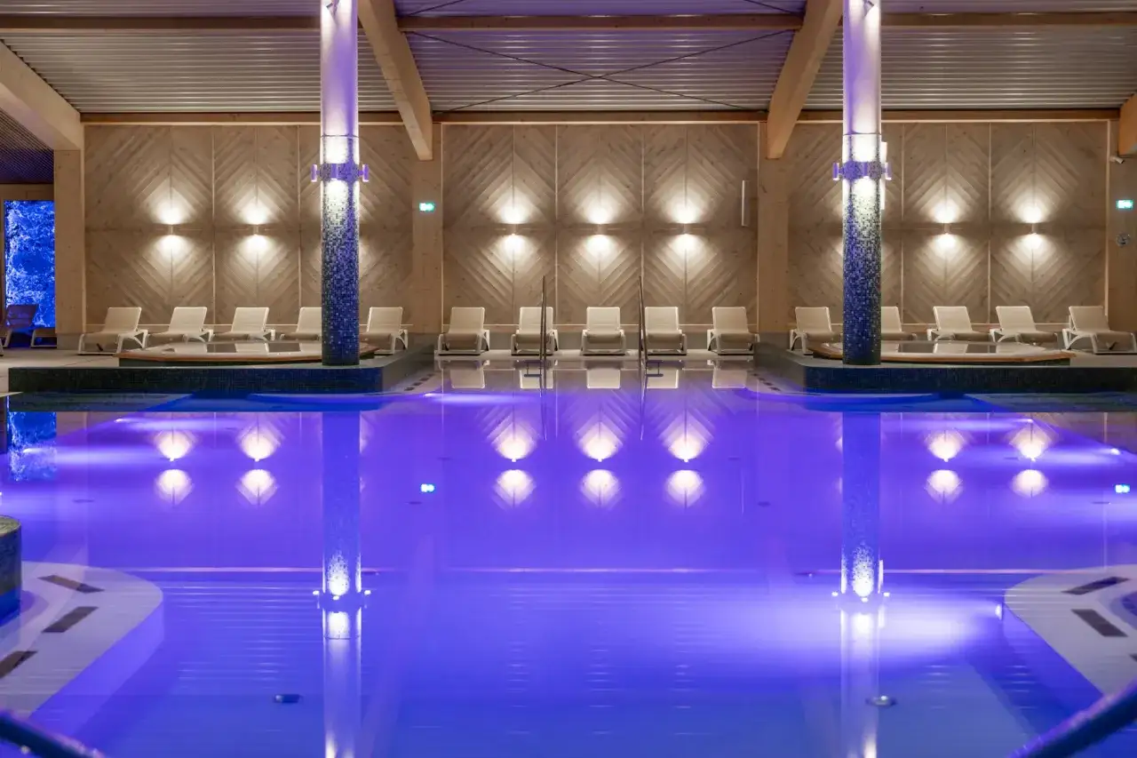 Relaks w basenie z niebieskim podświetleniem w Aries Szczyrk. Leżaki i jacuzzi czekają na gości.