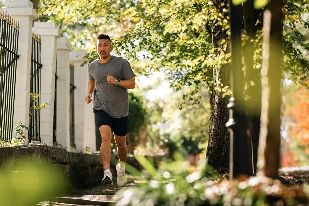 Ein Mann in Sportkleidung geht laufen, die Sonne scheint durch die B&auml;ume.
