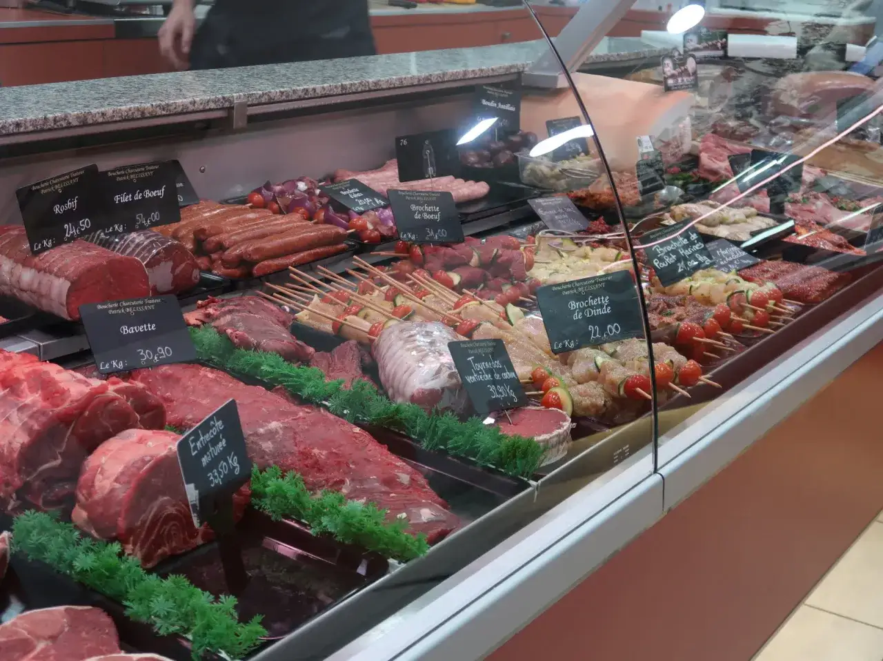 Vitrine de boucherie regorgeant de viandes fraîches, brochettes et saucisses. Une belle idée préparation boucherie pour un repas savoureux.
