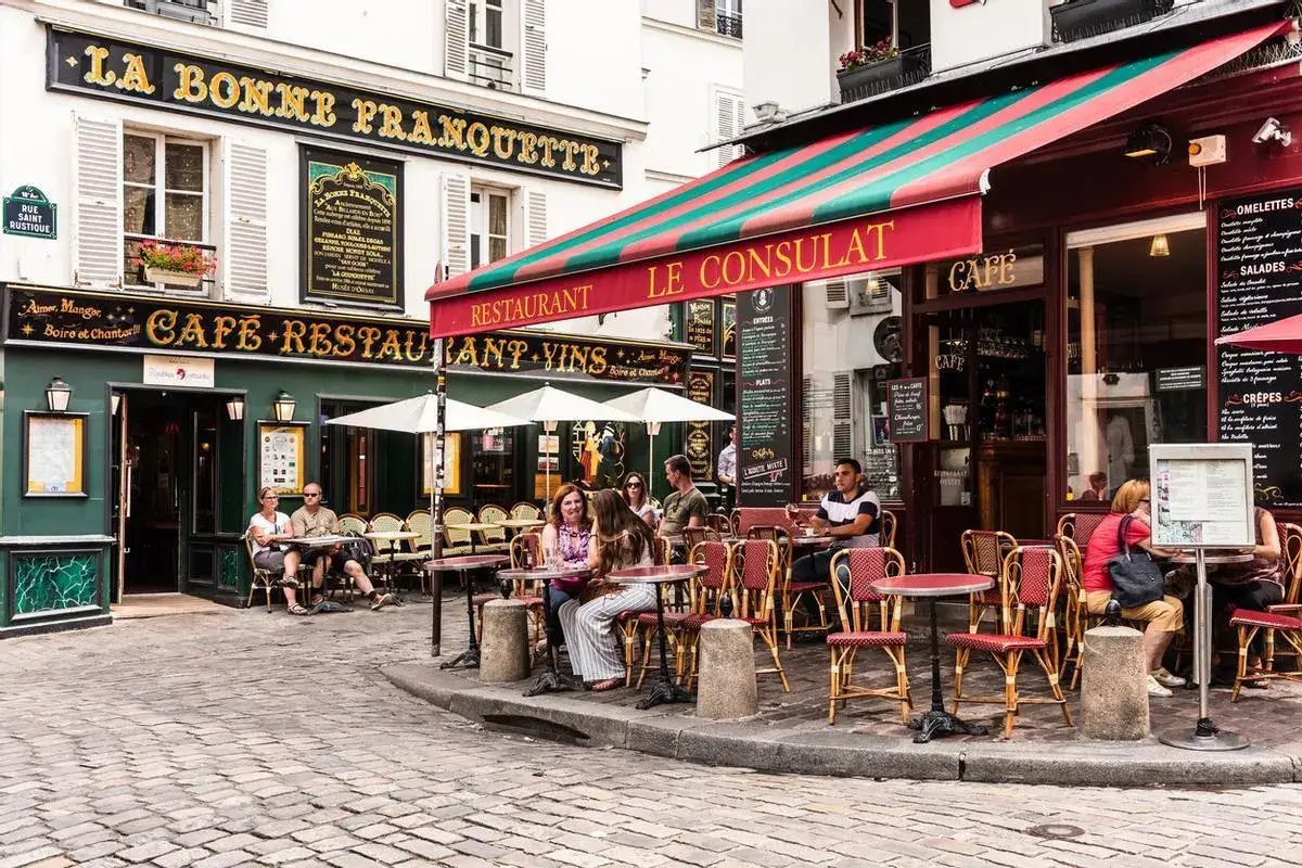 Cafés y restaurantes en una calle adoquinada de París, perfectos para saber dónde comer en París. Gente sentada en mesas al aire libre.