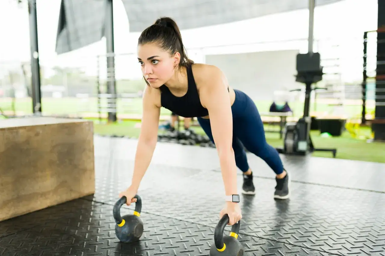 Frau in Plank-Position mit Kettlebells, trainiert ihre Bauchmuskeln.