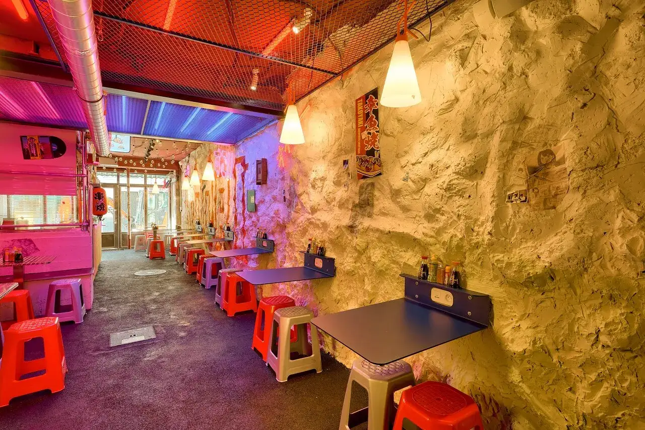 Ambiance n&eacute;on et rock dans ce restaurant **Noori Paris**. Tables pliantes, tabourets color&eacute;s et murs textur&eacute;s cr&eacute;ent un d&eacute;cor unique.