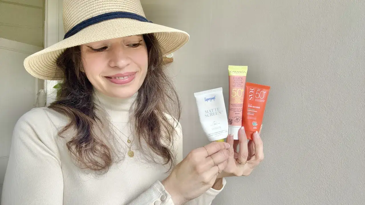 Une femme souriante, chapeau de paille, tient trois tubes de cr&egrave;me solaire. Le danger de la cr&egrave;me solaire tous les jours est une pr&eacute;occupation, mais ces produits offrent une protection SPF 50.