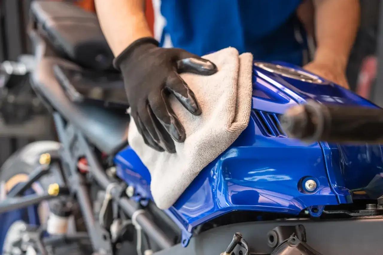 Mano enguantada limpia el depósito azul de una moto. Aprende cómo lavar una moto para que brille.