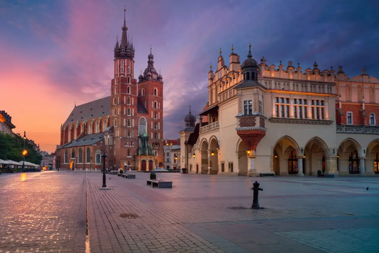 Krakowski rynek główny o wschodzie słońca. Bazylika Mariacka i Sukiennice w pastelowych barwach nieba.