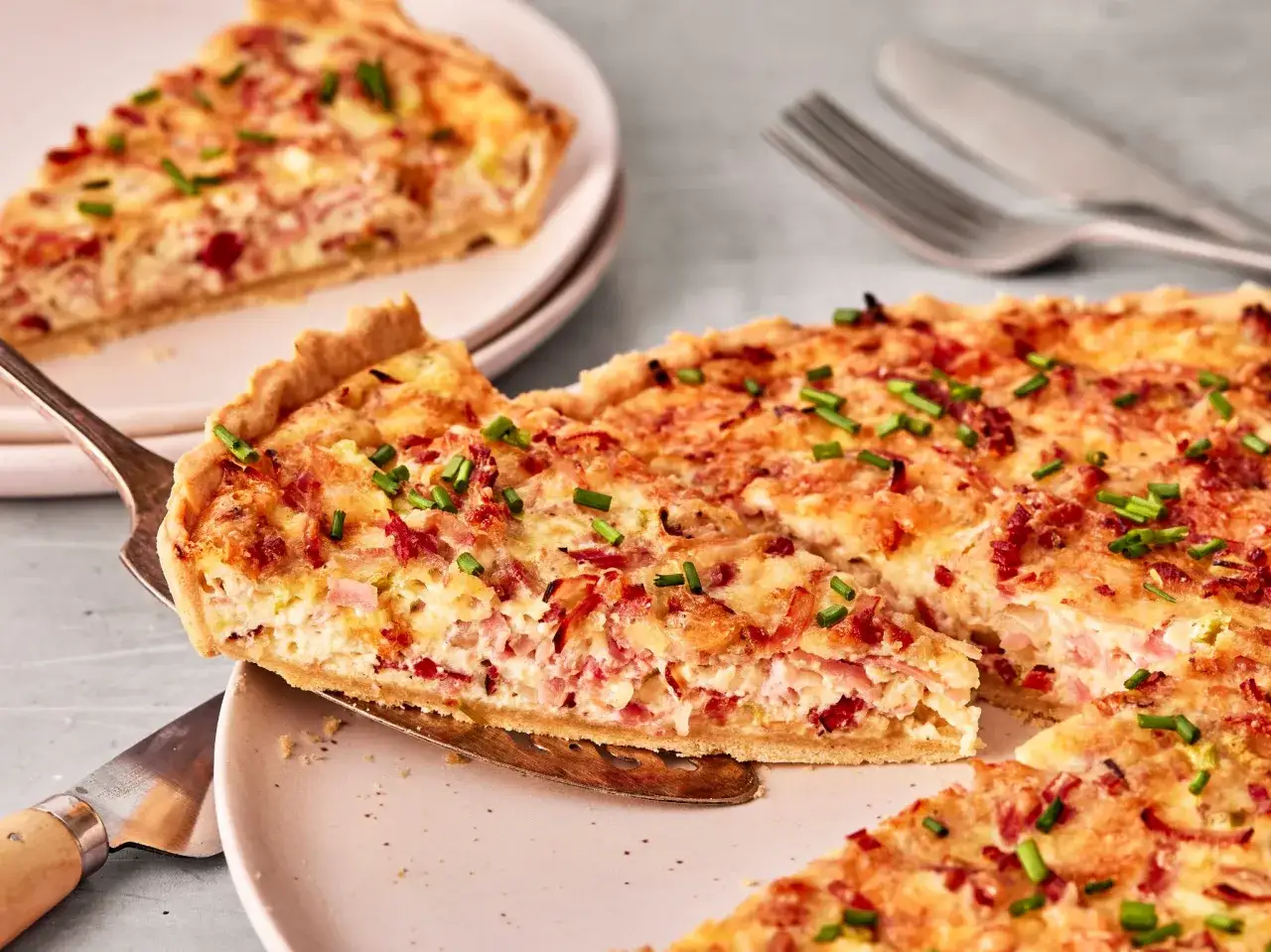 Herzhaftes Quiche Rezept mit Speck und Lauch, frisch aus dem Ofen. Ein Stück wird gerade serviert.